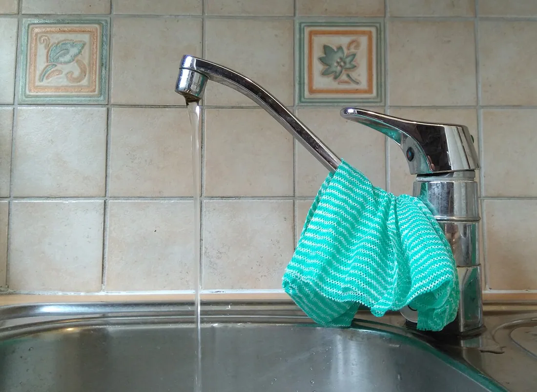Tap water running from kitchen tap. A rag sits drying on the tap. Фото: Fourteenzerozero / CC0, via Wikimedia…