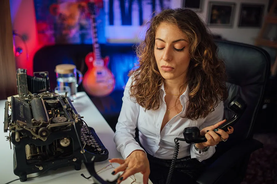 Businesswoman dialing numbers on a rotary phone next to an old typewriter. Фото: Shixart1985 / CC BY 2.0, via…