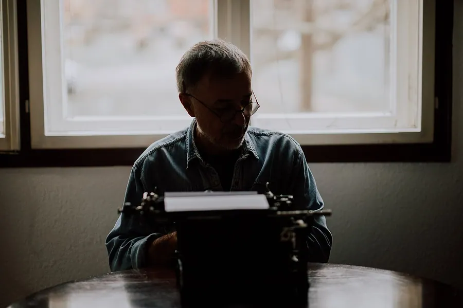 Senior man writer with glasses writing on an old typewriter.. Фото: Shixart1985 / CC BY 2.0, via Wikimedia…