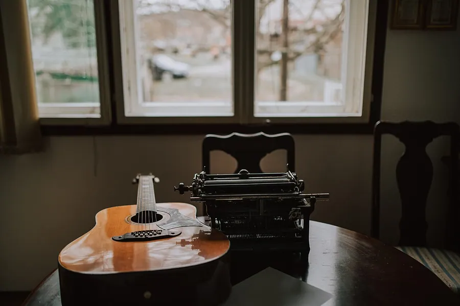 Old accoustic guitar and typewriter on the desk.. Фото: Shixart1985 / CC BY 2.0, via Wikimedia Commons