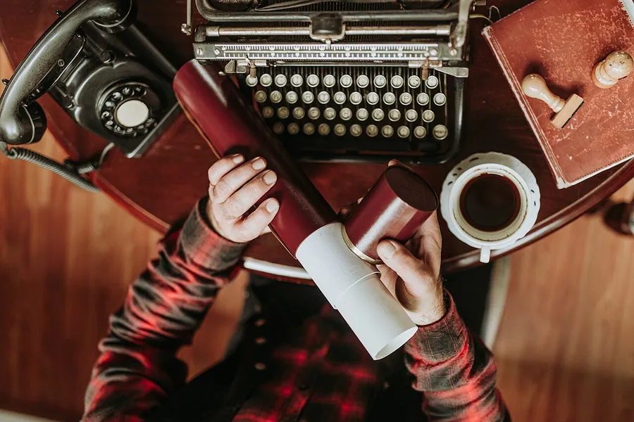 A workspace features a vintage typewriter, an old telephone, a cup of coffee, and two rolled papers. Фото…