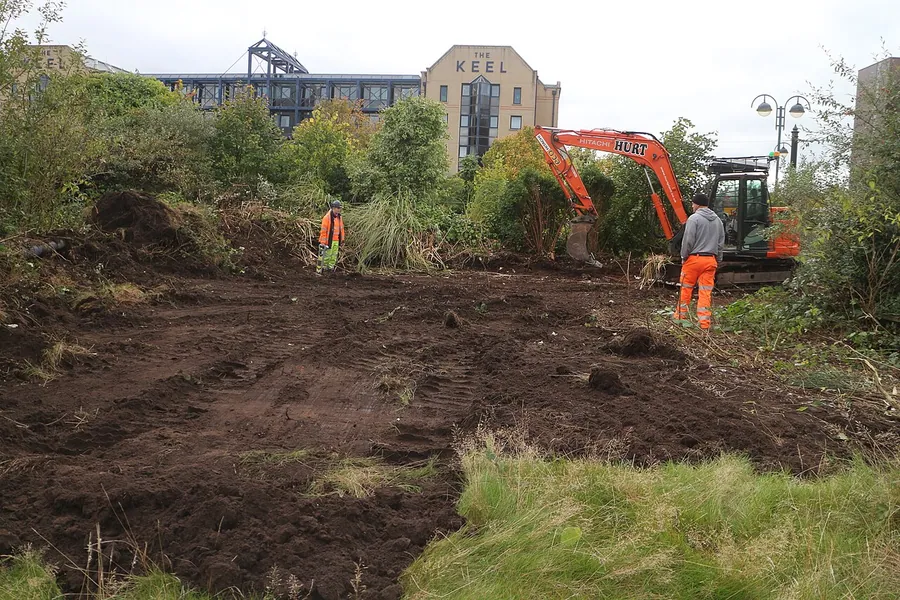 Two archaeologists observing an excavator digging in a wooded area.. Фото: Fraser Brown, Oxford Archaeology…